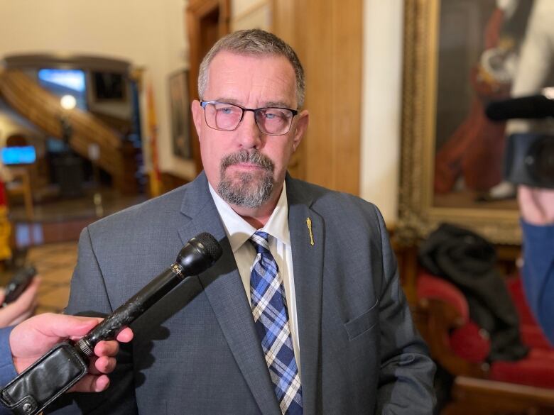  Man wearing glasses and a goatee stands in from of reporters at the legislature.