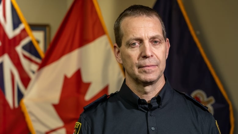 A man in uniform stands in front of the Canadian and British flag.