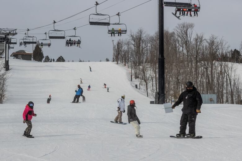 Multiple people are seen coming towards the camera skiing and snowboarding down a hill. 