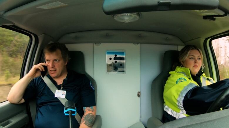 Two paramedics in driving down the road inside the cabin of an ambulance.