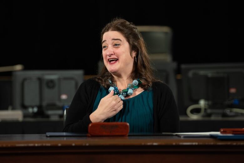 A politician smiles and gives a thumbs-up at a desk.