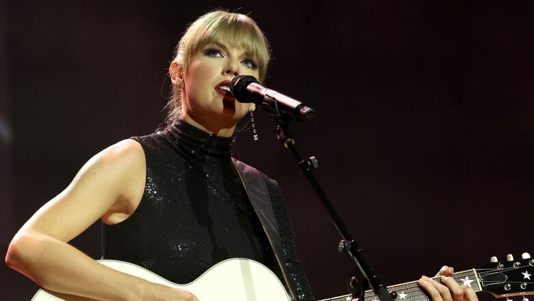 A woman holds a guitar and sings into a microphone. 