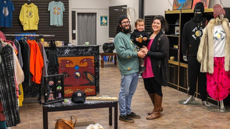 A man and woman stand in the middle of a store, smiling. They are holding their toddler between them.