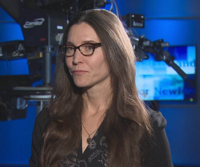  A woman with long brown hair and glasses sits in the CBC television studio.