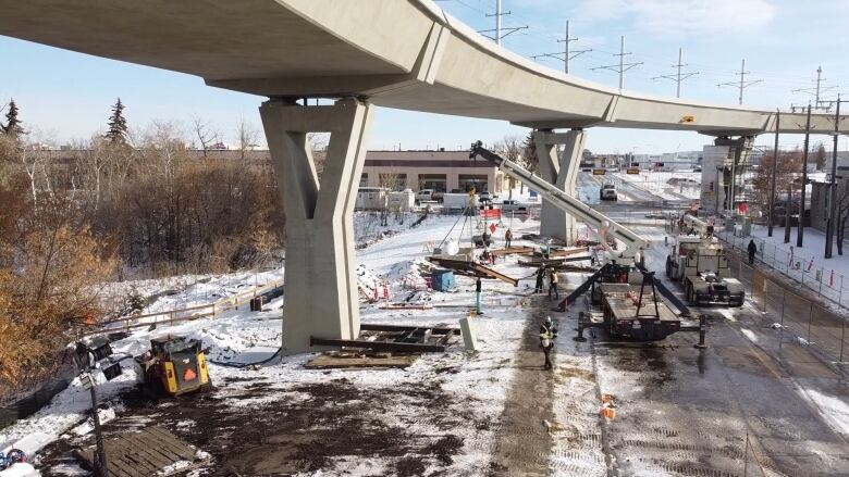 Workers and equipment at a construction site underneath an elevated train track.