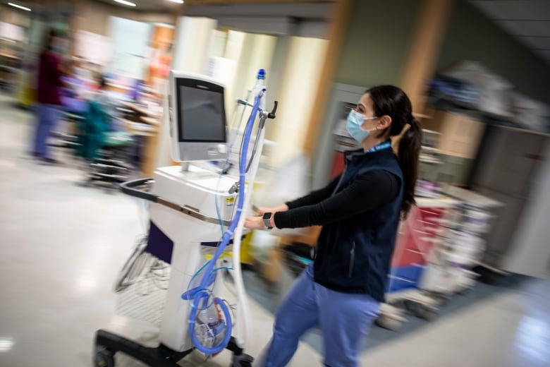 a doctor wearing a mask walks through a hospital wearing a mask and pushing a cart. 