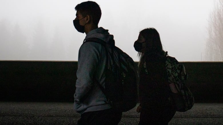 Two masked people walk next to each other in a corridor.