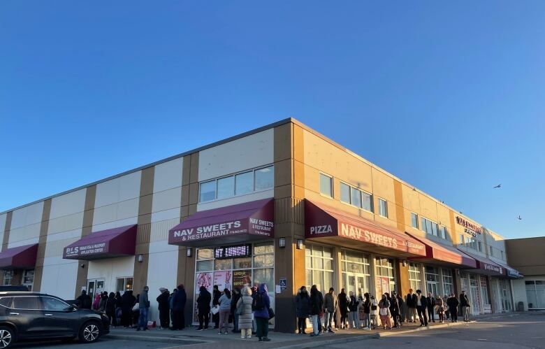 A lineup of people snaking around the block of a strip mall.