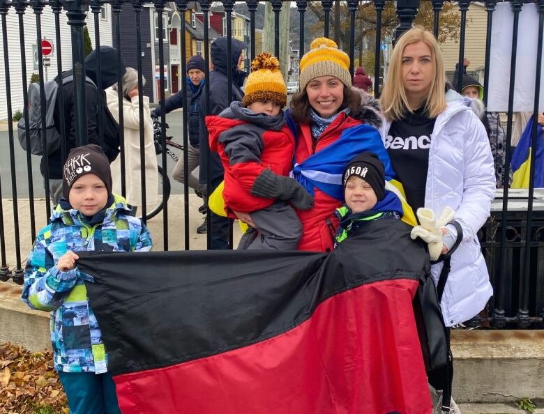 Women pose with their children outdoors holding flags and signs in the winter