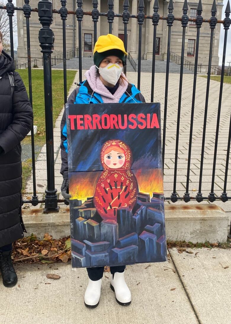 A woman wearing winter clothing stands outside holding up a handmade sign.