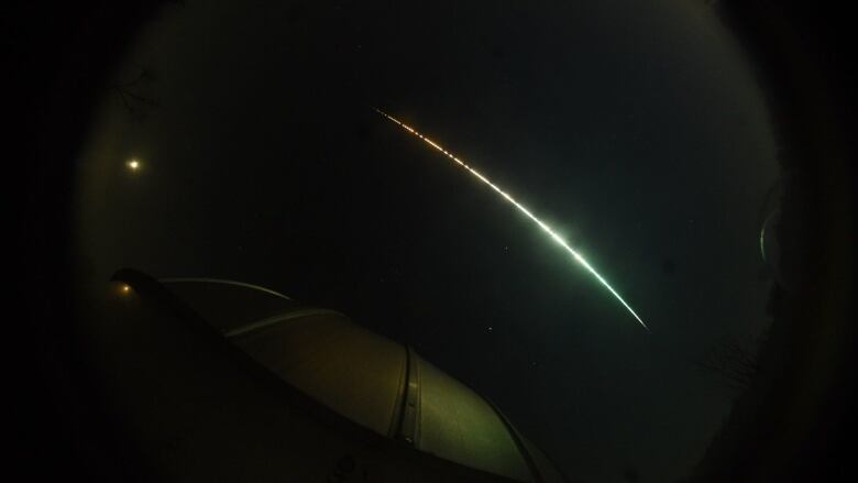 A meteor makes a white arc in the night sky. 