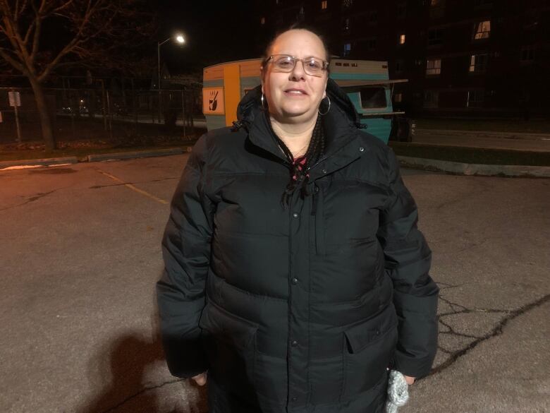 A woman wearing a black jacket and glasses on a dark street. 