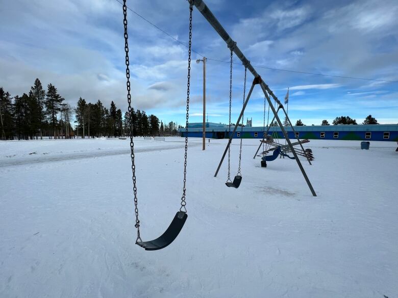 A swing set is seen in the snowy school yard of an elementary school painted in two tones of blue.