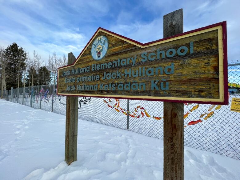 The sign for Jack Hulland Elementary School in Whitehorse, Yukon, is seen in front of a chain-link fence decorated with colourful artwork. 