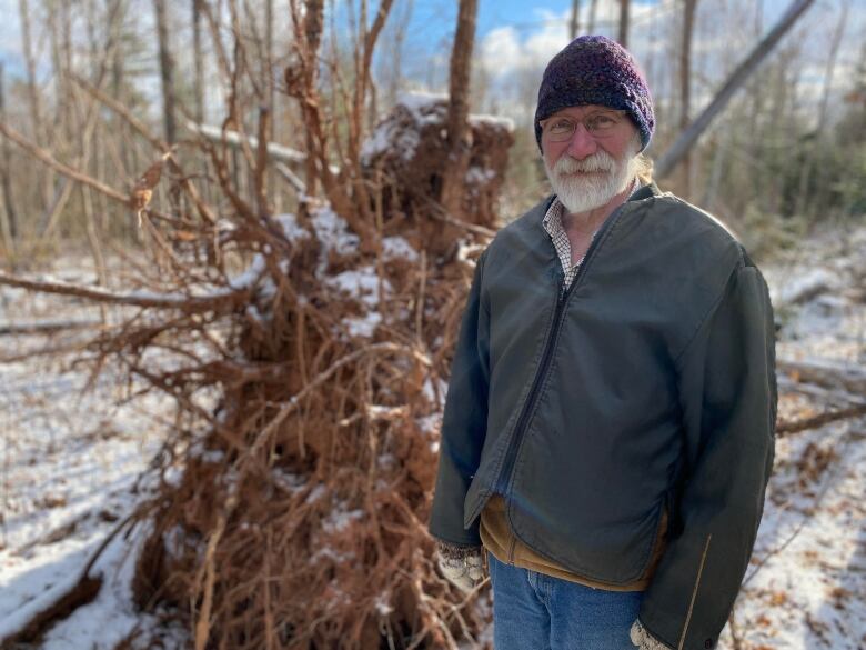 Man stands in front of forest debris with a light snow on the ground. 