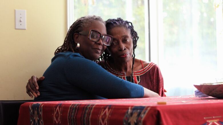 Two women sit at a red kitchen table.