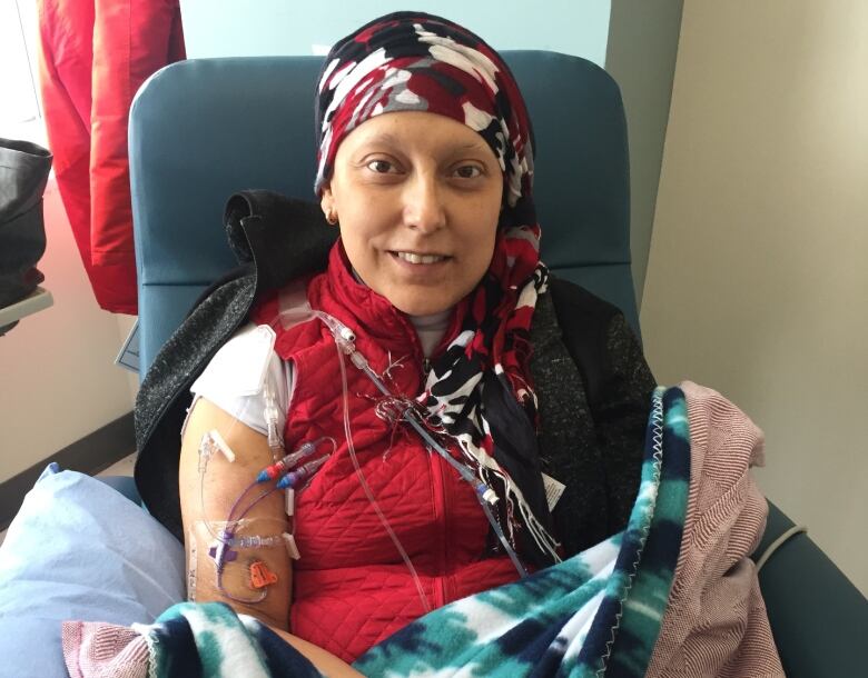 A woman's head is covered with a colourful scarf and there are needles for an IV drip in her arm, but she's smiling. 