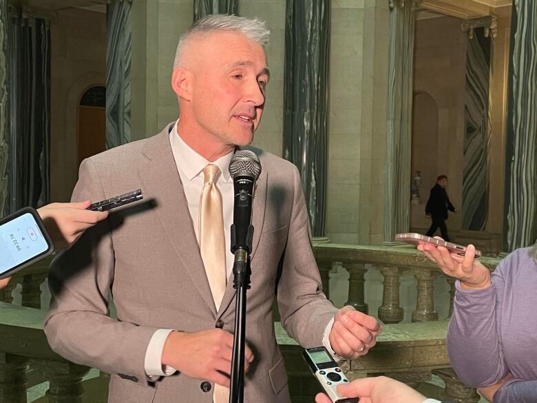 A white man in a grey suit and grey hair is speaking to reporters in a rotunda.