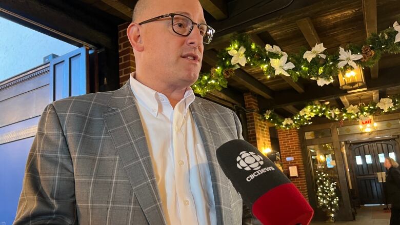 A bald man in a suit stands in front of white flower garlands. 