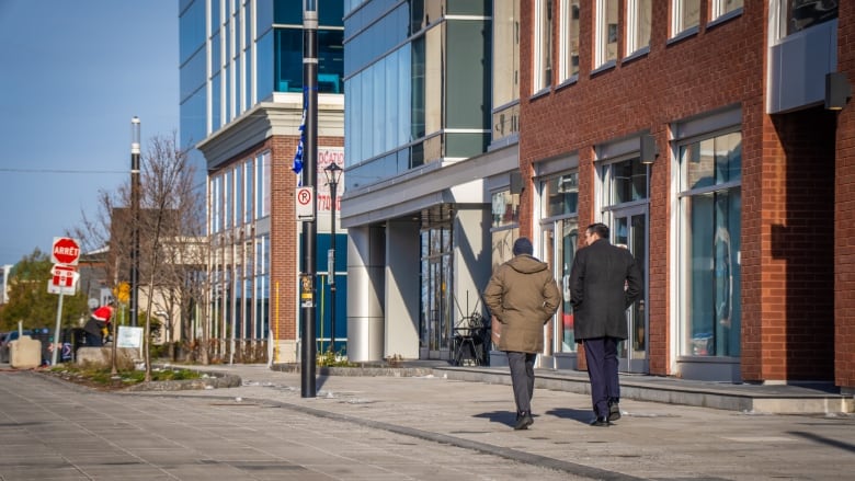 Two people walk down a quiet city street in late autumn.