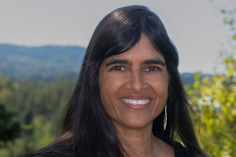 Anjali Oberai smiling at camera. Trees and sky in the background. 