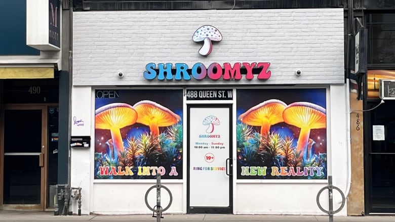 A mushroom logo and a sign that reads Shroomyz is pictured on a white brick storefront. 