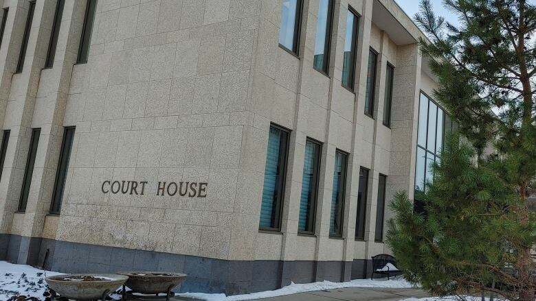 A stone building features gold letters that read, 'Court House.' A fir tree stands in front of the building. There is light snow on the ground, but the walkway is clear.