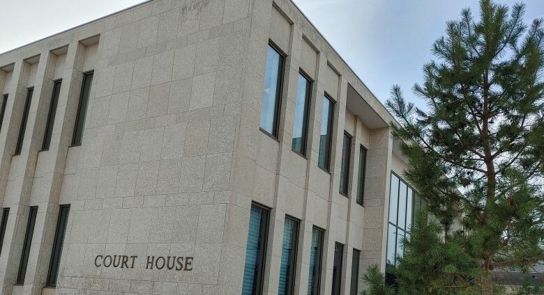 A stone building features gold letters that read, 'Court House.' A fir tree stands in front of the building. There is light snow on the ground, but the walkway is clear.