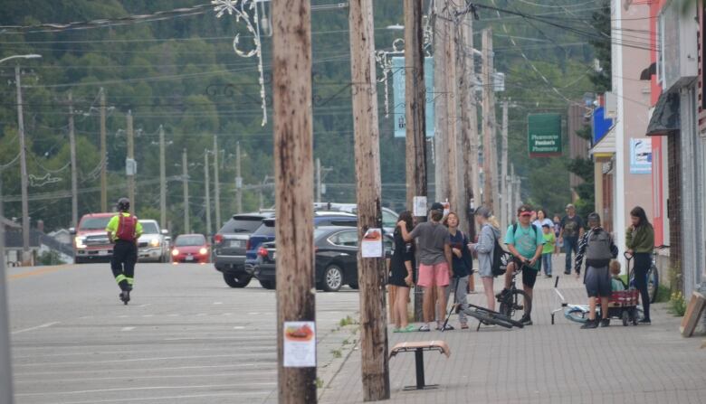 Summer scene on Main Street in Wawa showing kids on a sidewalk next to a pile of bikes, telephone phones, parked cars and a man riding a scooter down the street