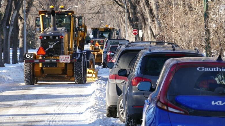 An orange grader travels up a Winnipeg residential street clearing snow.