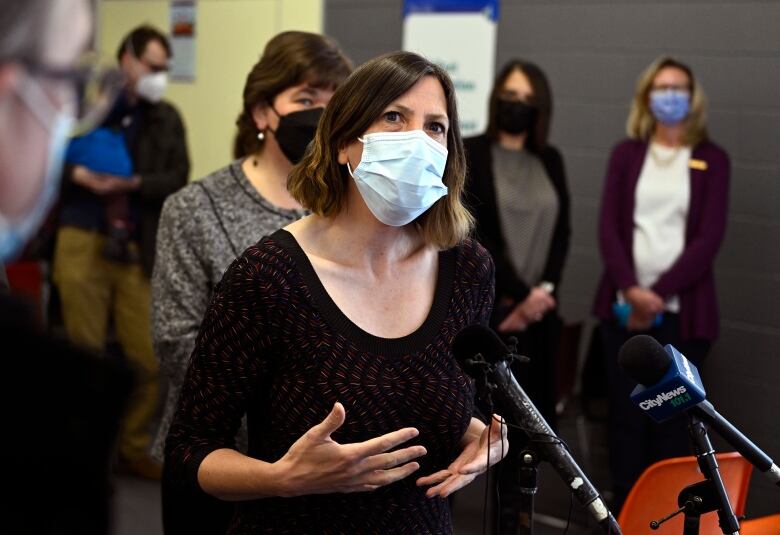 A health official in a mask speaks into a microphone.