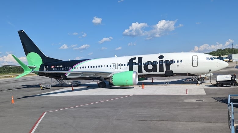 A white large-body plane with a black tail and green accents sits on the runway.