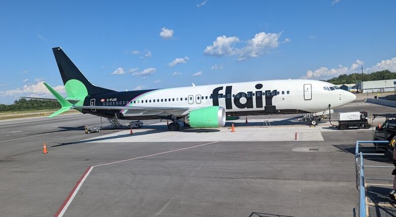 A white large-body plane with a black tail and green accents sits on the runway.