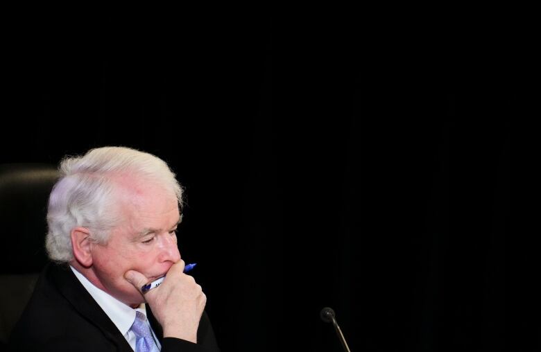 A man pauses to think, in front of a microphone.