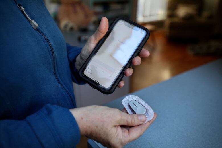 A person's hands hold a smartphone and a sensor used for continuous glucose monitoring.