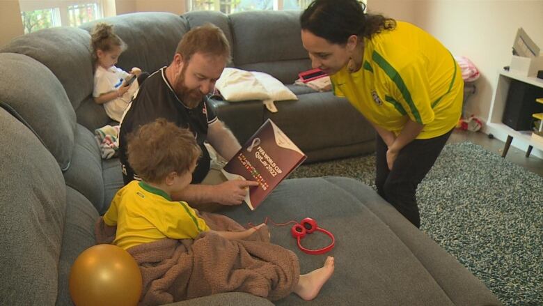 A man points to a sticker book next to a small boy. A woman looks at the boy.