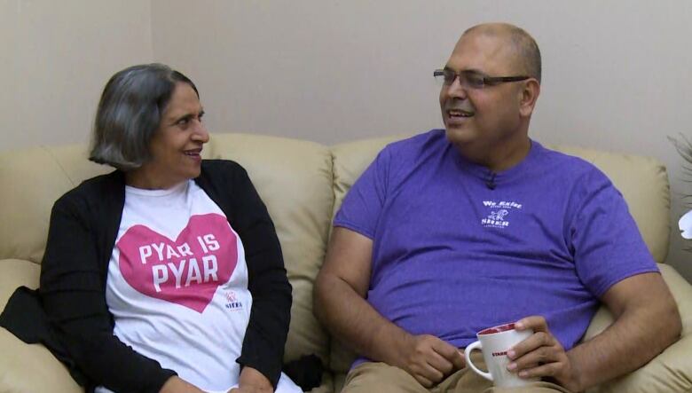 Two South Asian people smile while sitting on a couch.