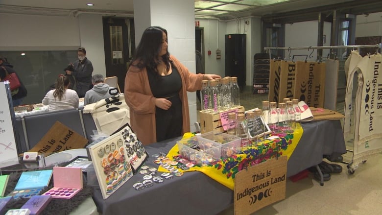 Person standing behind a table filled with various wares.