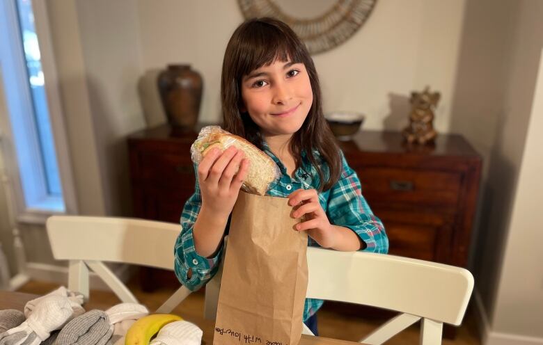 Girl holding sandwich and paper bag.