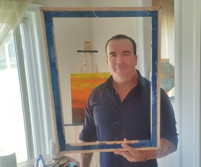 Man holds blue, empty rectangle frame in front of him.