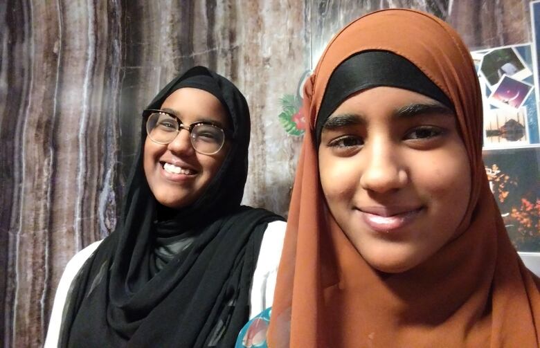 Smiling twin teenage Muslim girls wearing hijabis smile for a photo.