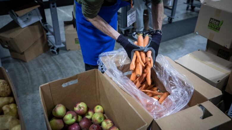 Carrots are removed from a box. Next to them are apples in another box.