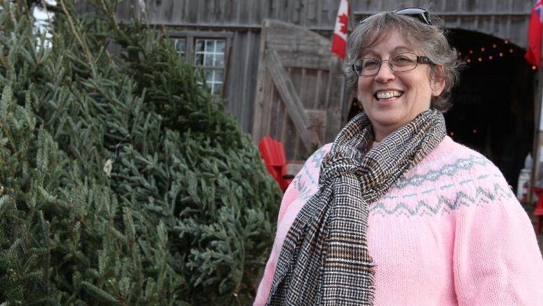 Individual in a pink sweater and scarf smiling broadly beside a Christmas tree.