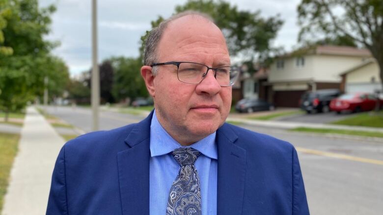 man in blue suit stands on sidewalk looking off camera