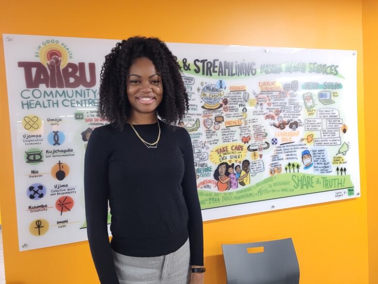 Woman standing in front of a poster for TAIBU Community Health Centre.