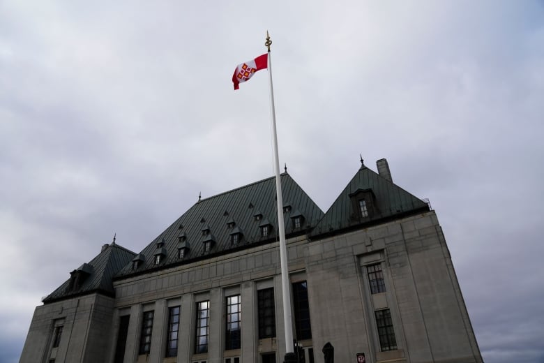 A red, white and gold flag flies over a large courthouse.