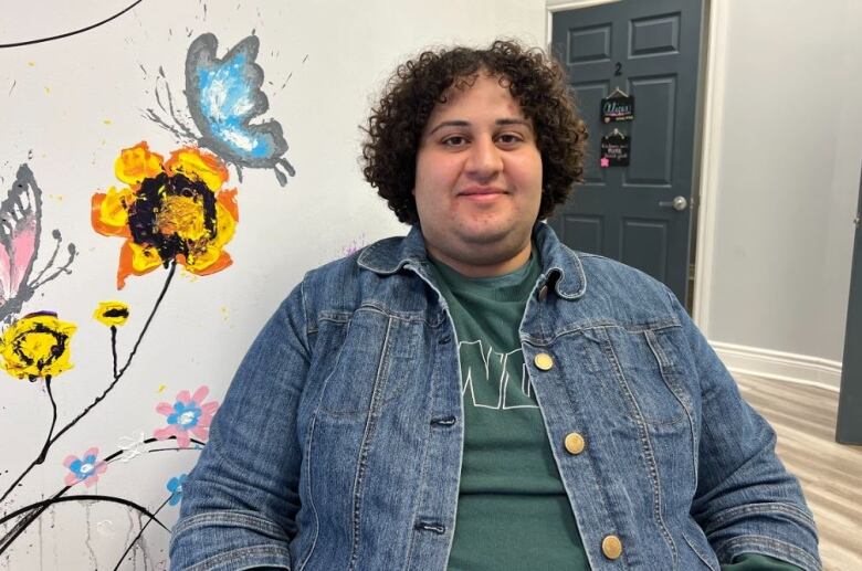 A person sits down in front of a wall with a painted flower and butterfly.