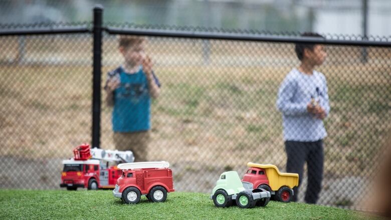 Children's toys in the foreground with children behind a fence in the background. 