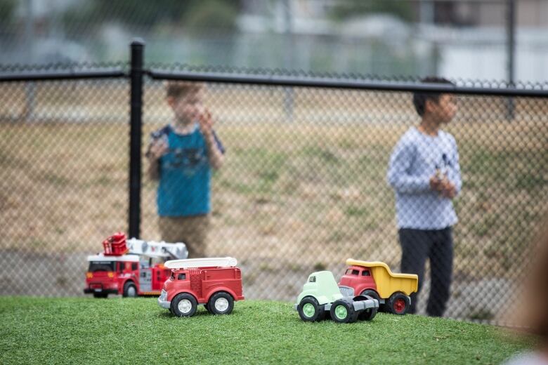 Children's toys in the foreground with children behind a fence in the background. 