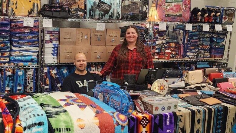 A woman and man stand behind tables of brightly coloured textile products.